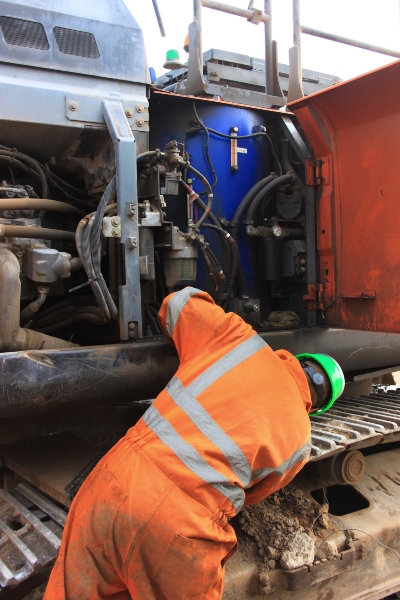 Engineer in hi vis overalls and green hard hat inspecting a demolition machine for leaks.