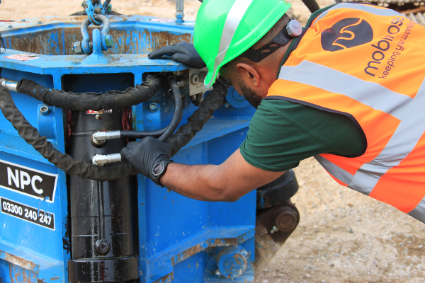 Repaired hose on blue demolition muncher being inspected by engineer.