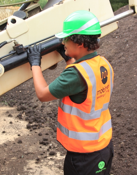 Young person in high vis jacket and hard hat inspecting a hydraulic ram.