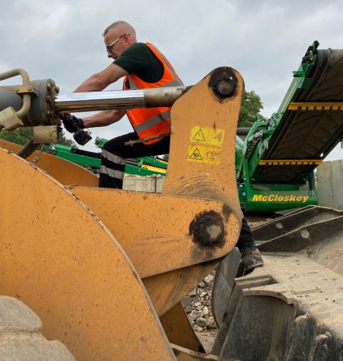 Engineer in high vis jacket on a piece of machinery repairing a hydraulic ram.